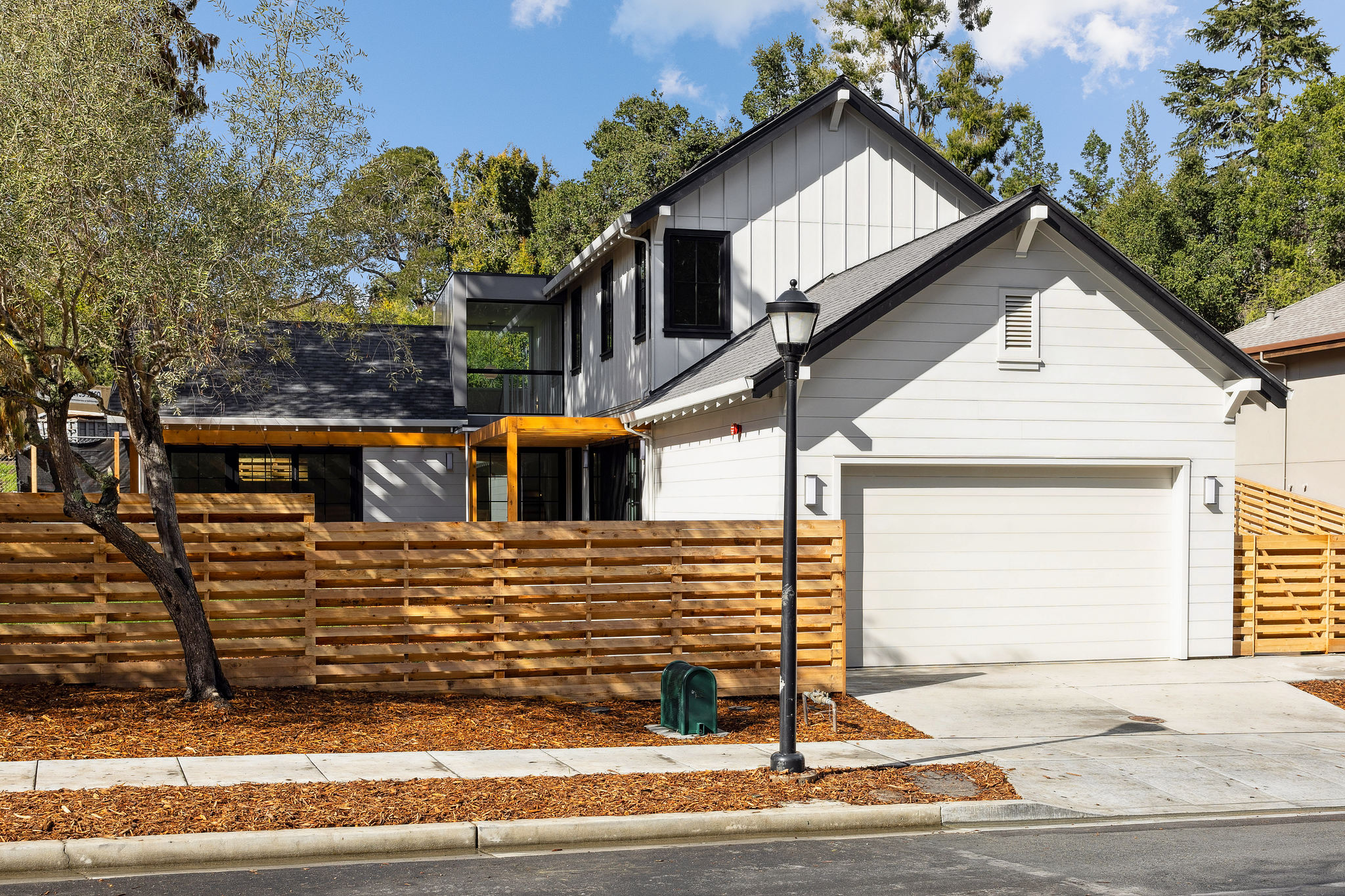 Front of 2-story white home with wooden fence and 2-car garage.
